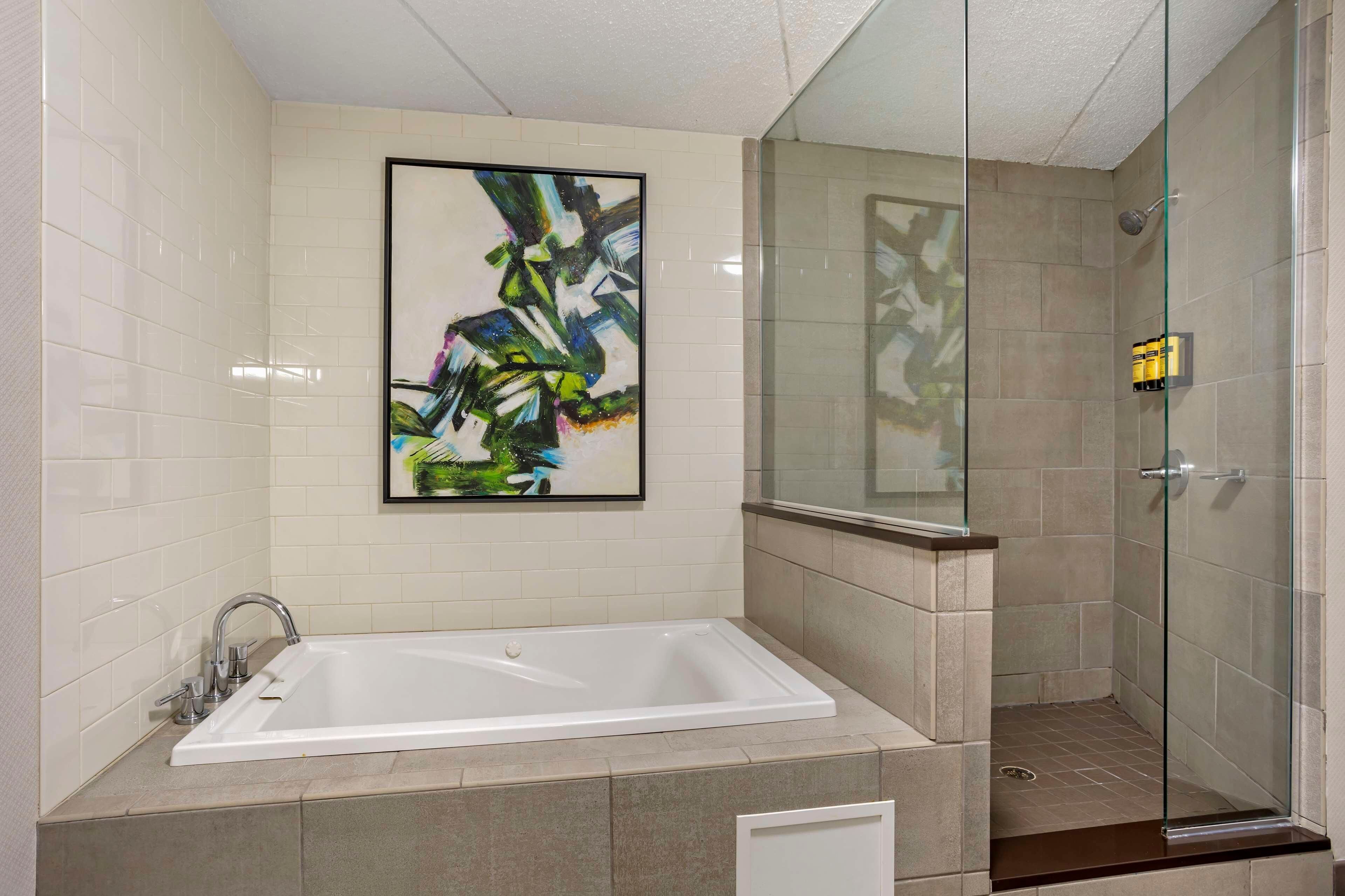 A modern bathroom with a large bathtub, a glass shower enclosure, and a framed abstract painting on the wall.