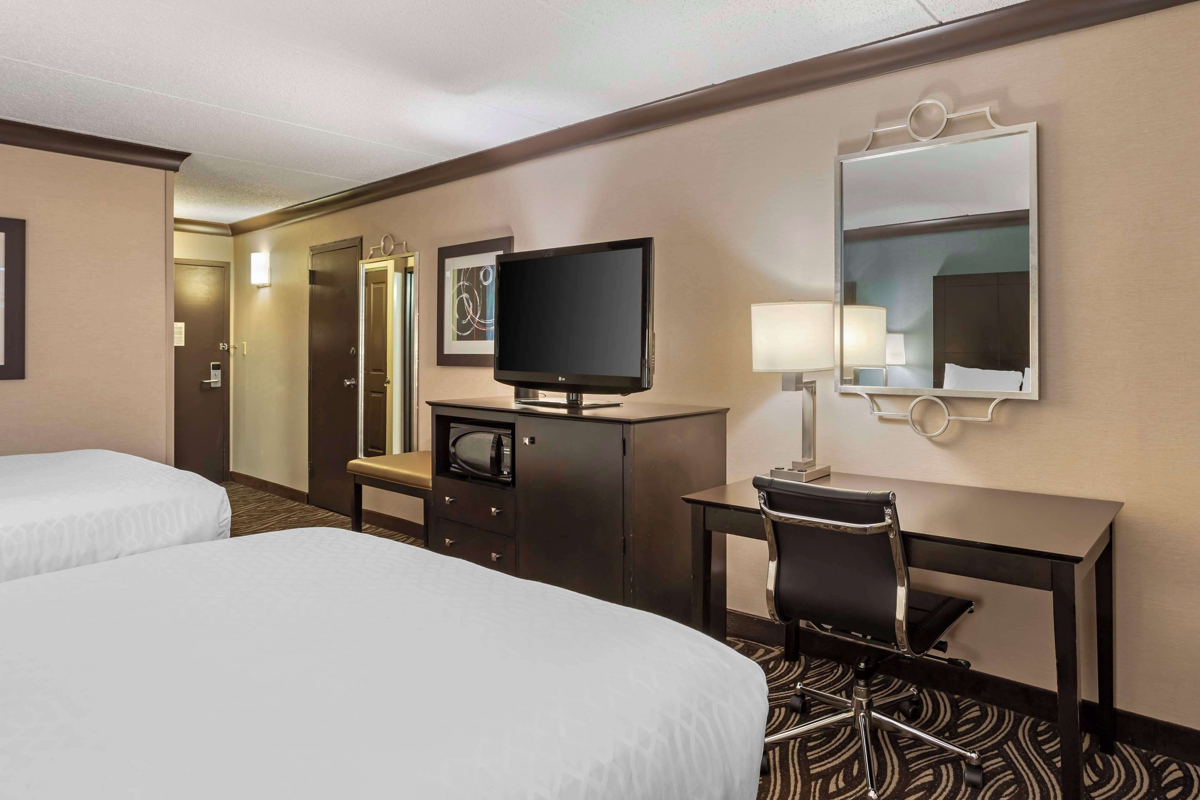 A hotel room with two beds, a desk, a television, a desk lamp, and a mirror.
