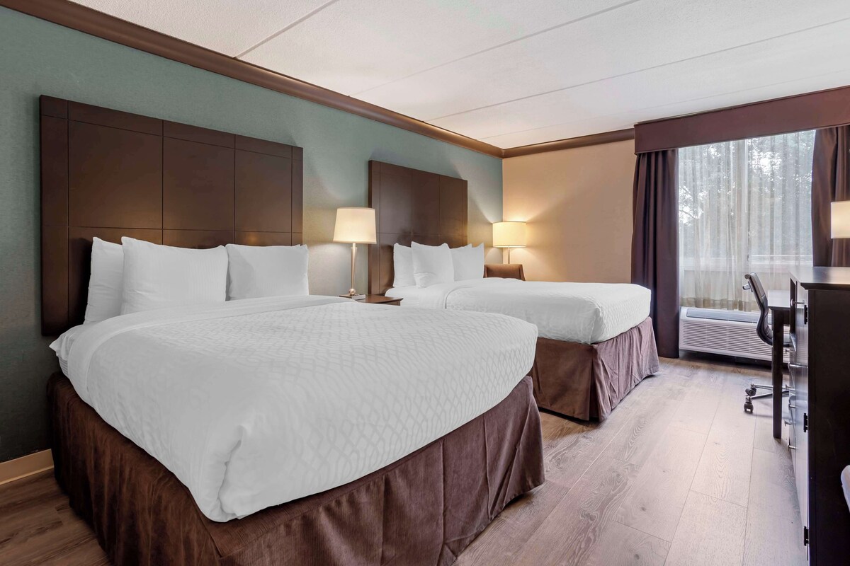 A hotel room with two beds, a desk, and a large window.