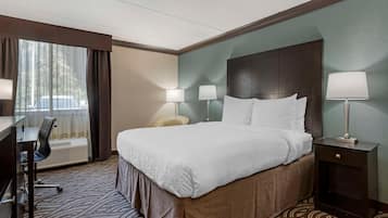 Una habitación de hotel con una cama grande, un escritorio con silla, dos lámparas de noche y un ventanal con cortinas.