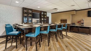 A bar area with a long counter, multiple bar stools, and a television mounted above the bar.