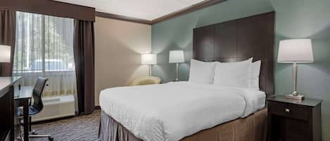 Habitación de hotel con una cama grande, dos lámparas de noche, un escritorio con silla y vistas a árboles desde la ventana.