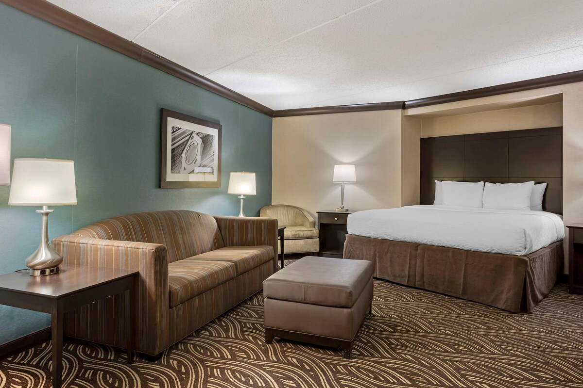A hotel room with a bed, a sofa, an ottoman, two lamps, a chair, and a framed picture on the wall.