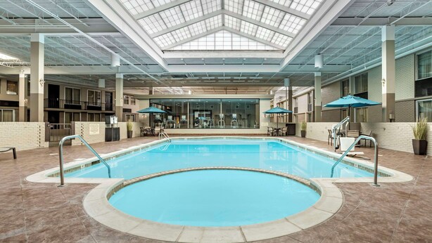 A swimming pool with a glass ceiling, indoor seating, and a brick wall.
