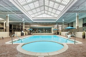 A swimming pool with a glass ceiling, indoor seating, and a brick wall. - Kingston Regency Inn (Kingston)