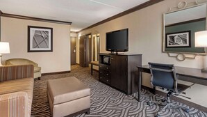 A hotel room with a sofa, ottoman, desk, chair, television, and a mirror.