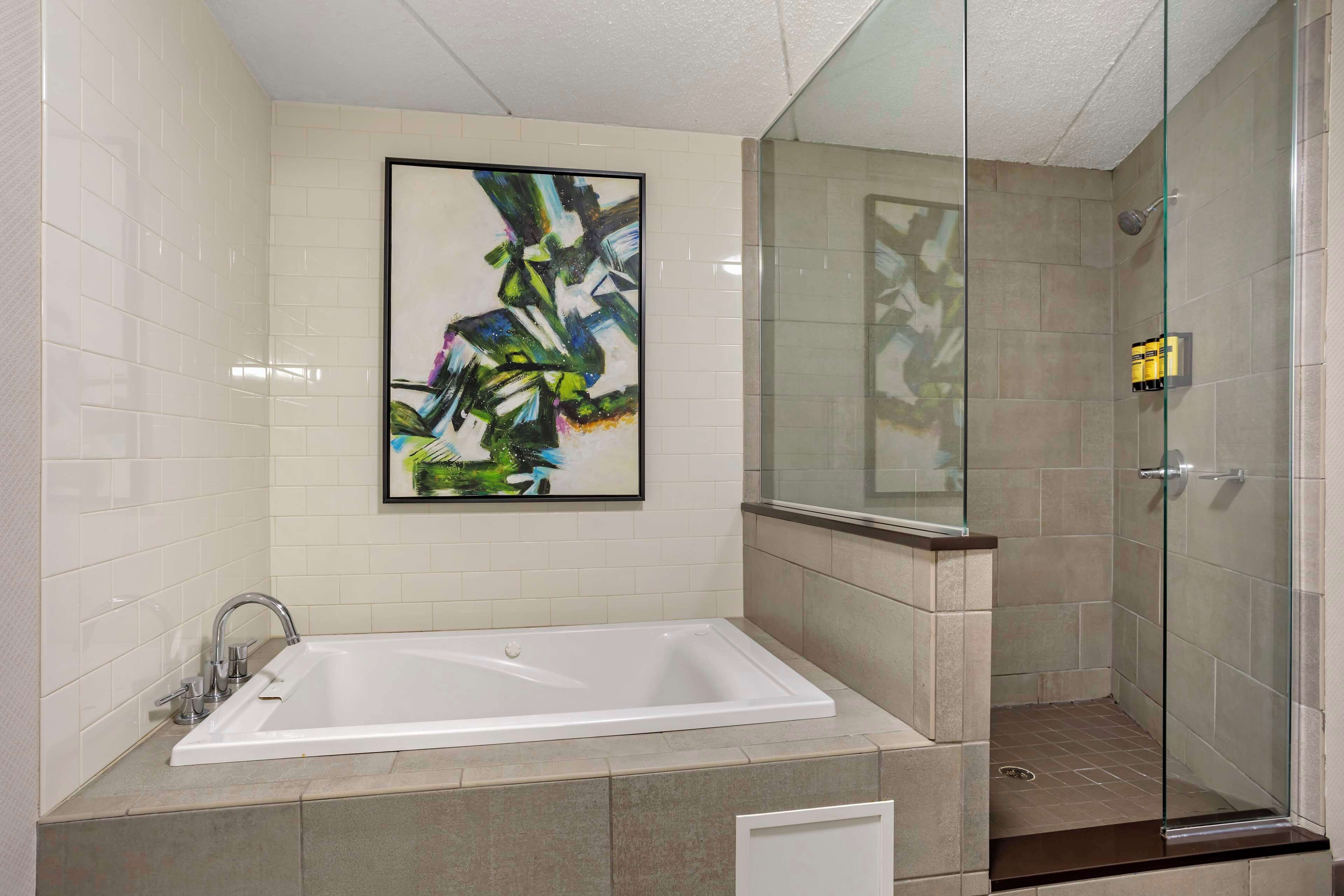 A modern bathroom with a large bathtub, a glass shower enclosure, and a framed abstract painting on the wall.