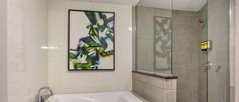 A modern bathroom with a large bathtub, a glass shower enclosure, and a framed abstract painting on the wall.