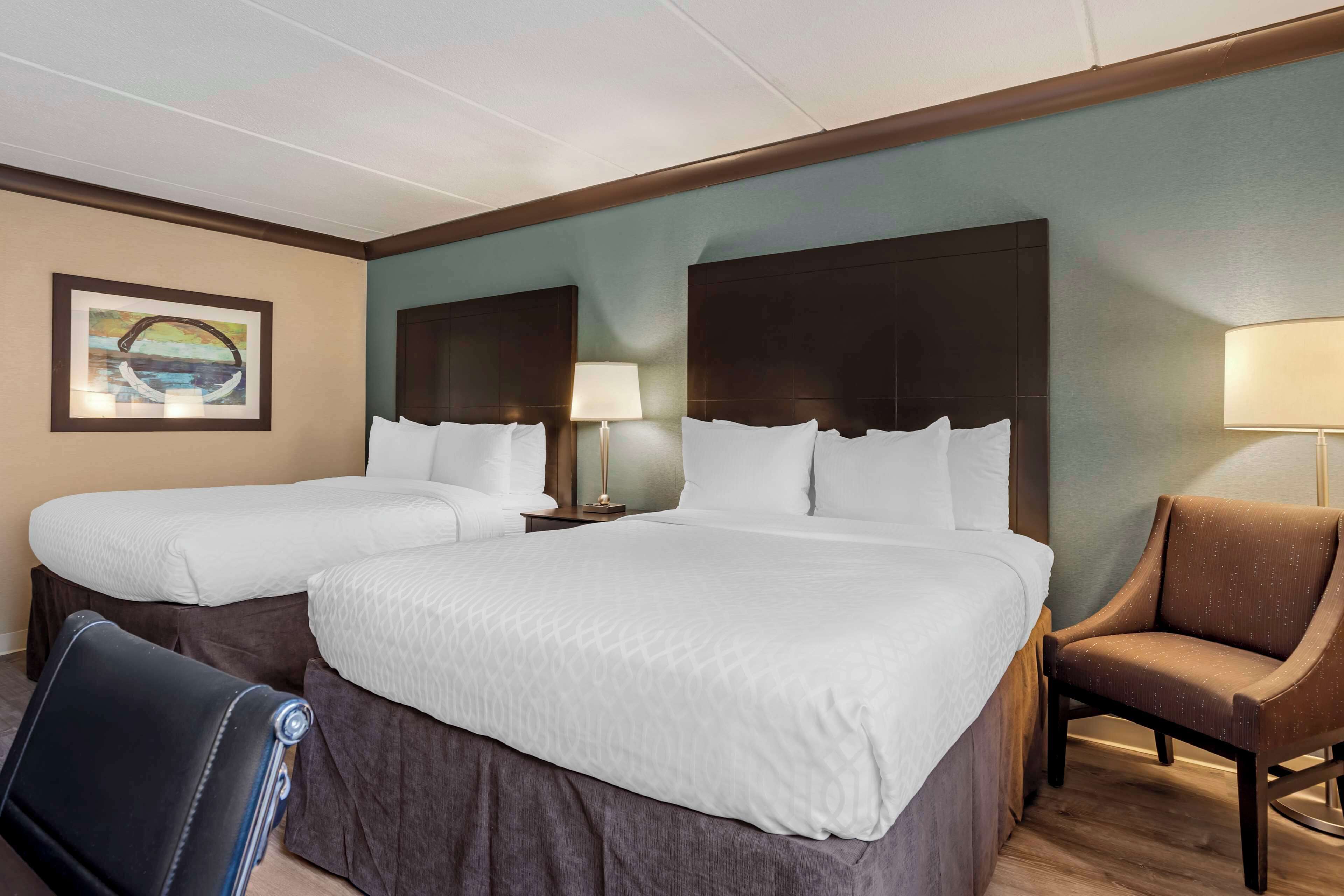 A hotel room with two beds, a chair, and a lamp.