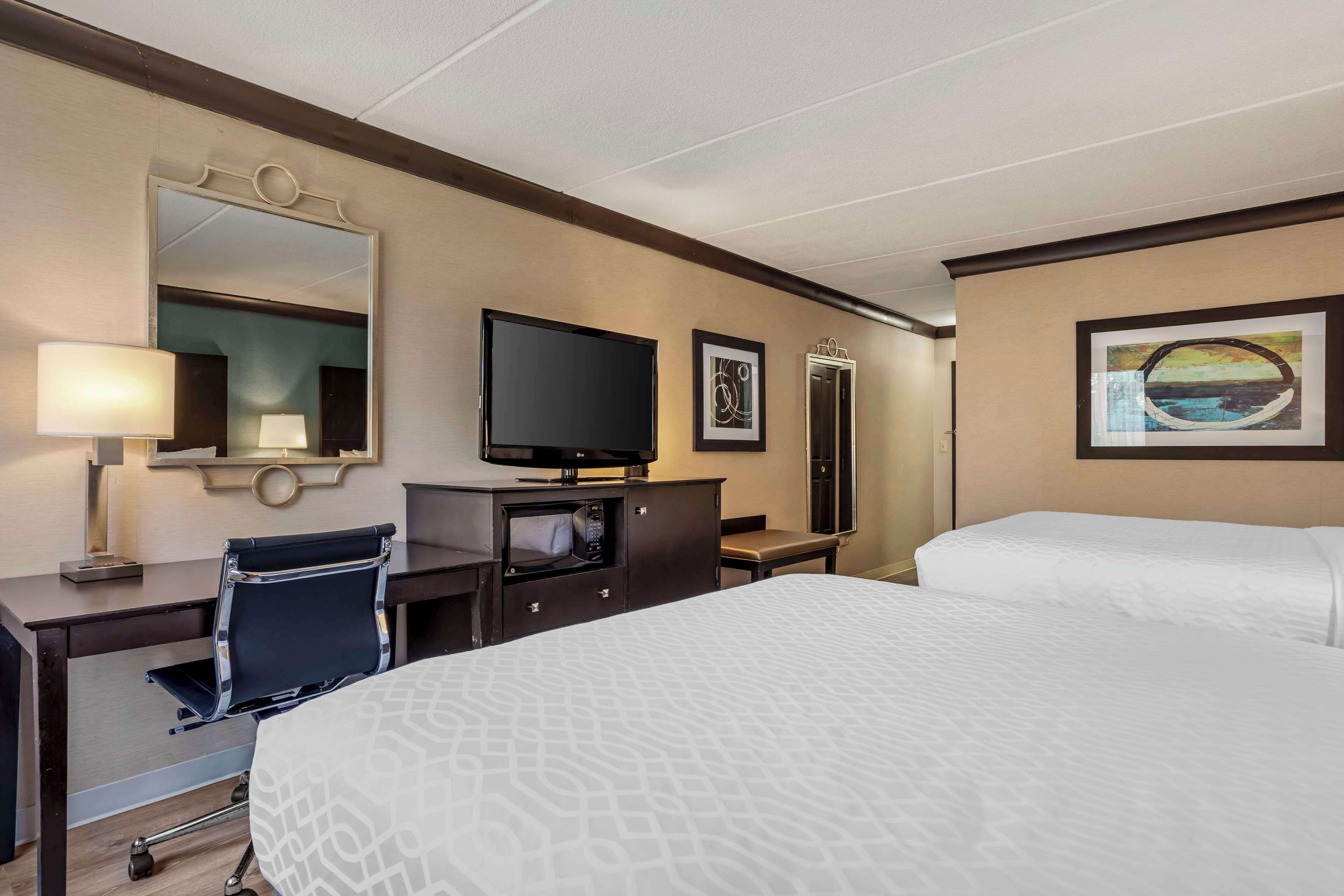 Quarto de hotel com uma cama grande, uma escrivaninha com cadeira, televisão, micro-ondas e espelho.