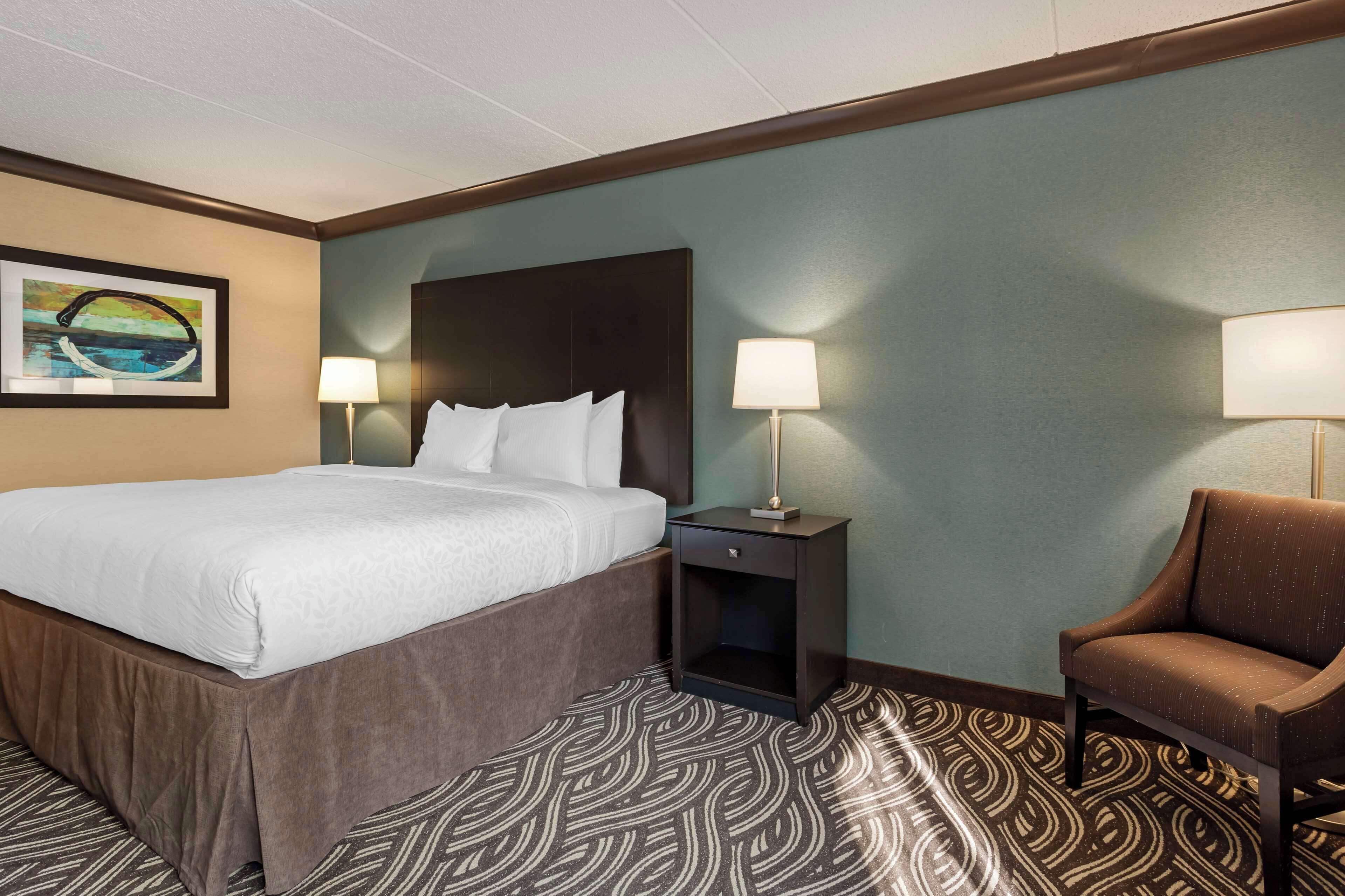 A hotel room with a bed, two bedside tables with lamps, a chair, and a patterned carpet.