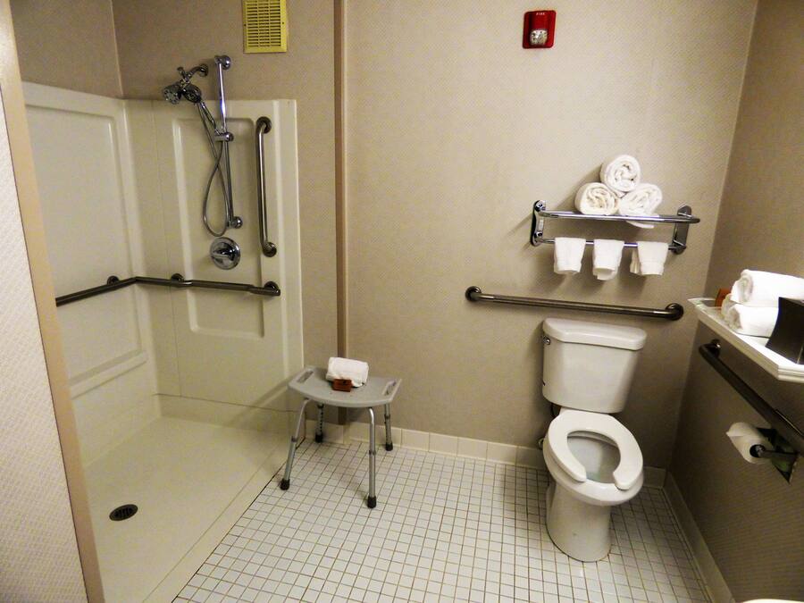 Un baño con cabina de ducha a ras de suelo, barras de apoyo, inodoro y un lavabo pequeño.