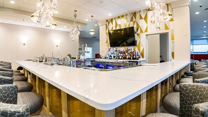 A bar area with a long counter, bar stools, and a television screen. - Sheraton Richmond Airport Hotel (Sandston)