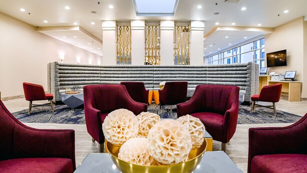 A lobby with red chairs, a gold bowl of decorative items, and a seating area with a patterned rug. - Sheraton Richmond Airport Hotel (Sandston)