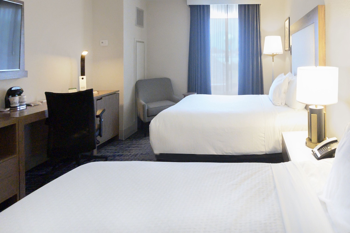 Une chambre d’hôtel avec deux lits, un bureau avec une lampe, une chaise et une table de chevet avec un téléphone.