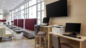 A modern hotel lobby with a long reception desk, multiple seating areas, and large windows providing natural light.