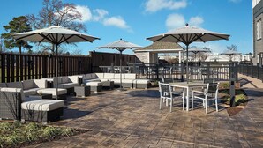 An outdoor patio area with a seating arrangement, including sofas and a table with chairs, shaded by large umbrellas. - Sheraton Richmond Airport Hotel (Sandston)