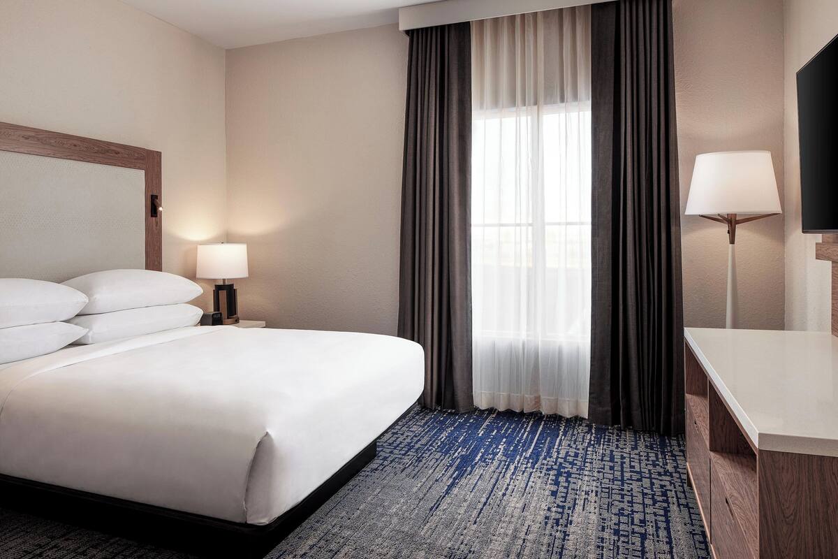 Una habitación de hotel con una cama grande, un escritorio, un televisor y una ventana con cortinas.
