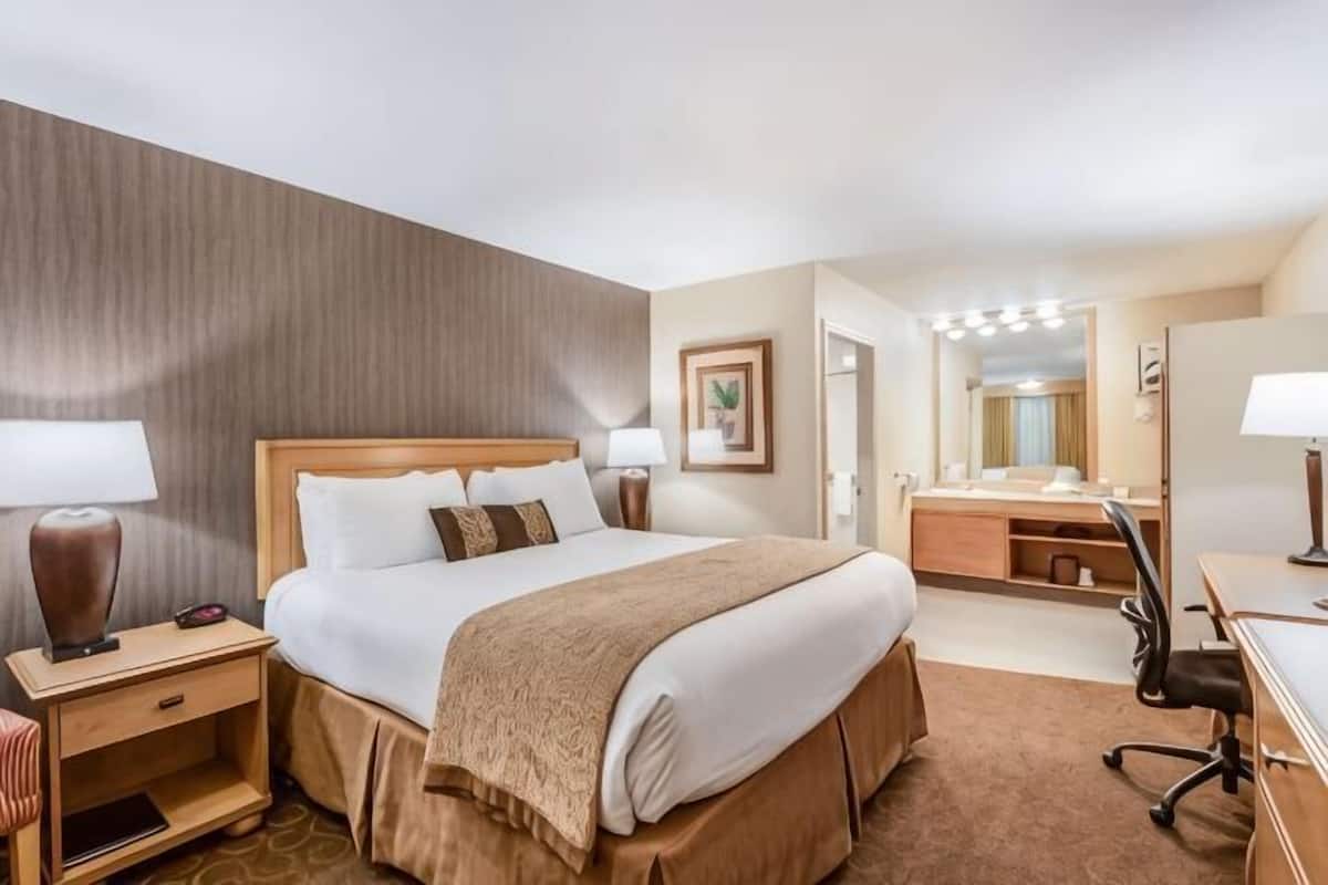 A hotel room with a large bed, bedside tables, a desk, a chair, a mirror, and a vanity with a mirror.