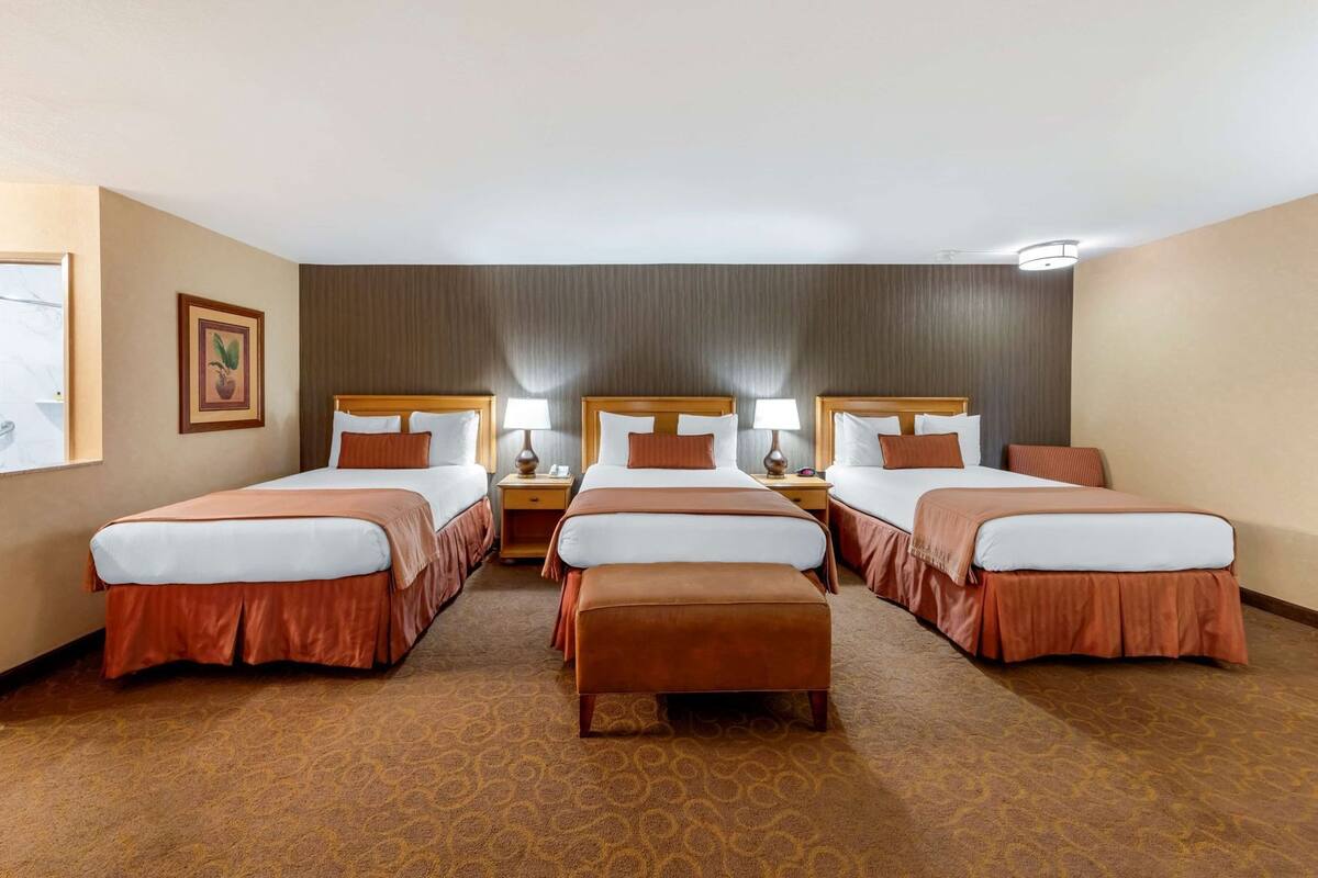Een hotelkamer met vier bedden op rij, een tafeltje tussen de bedden en een foto aan de muur.