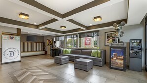 A hotel lobby with a large sofa, ottomans, a reception desk, and a Disneyland sign.