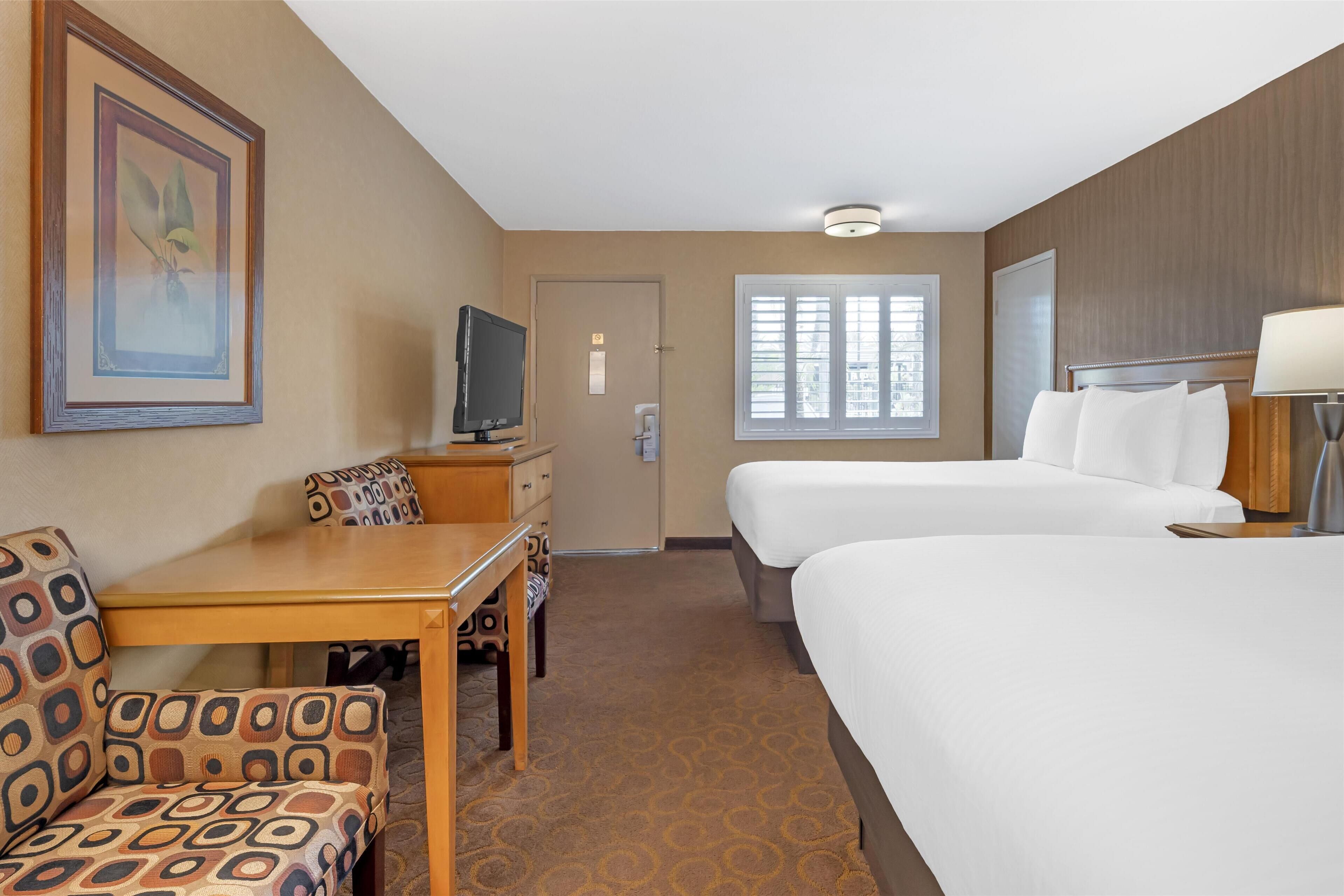 Une chambre d’hôtel avec un lit, un bureau, une chaise, une télévision et une fenêtre.