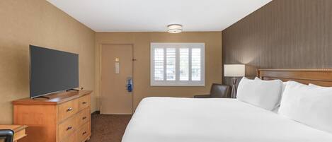 A hotel room with a large bed, a wooden dresser, a television, a window, and a door.