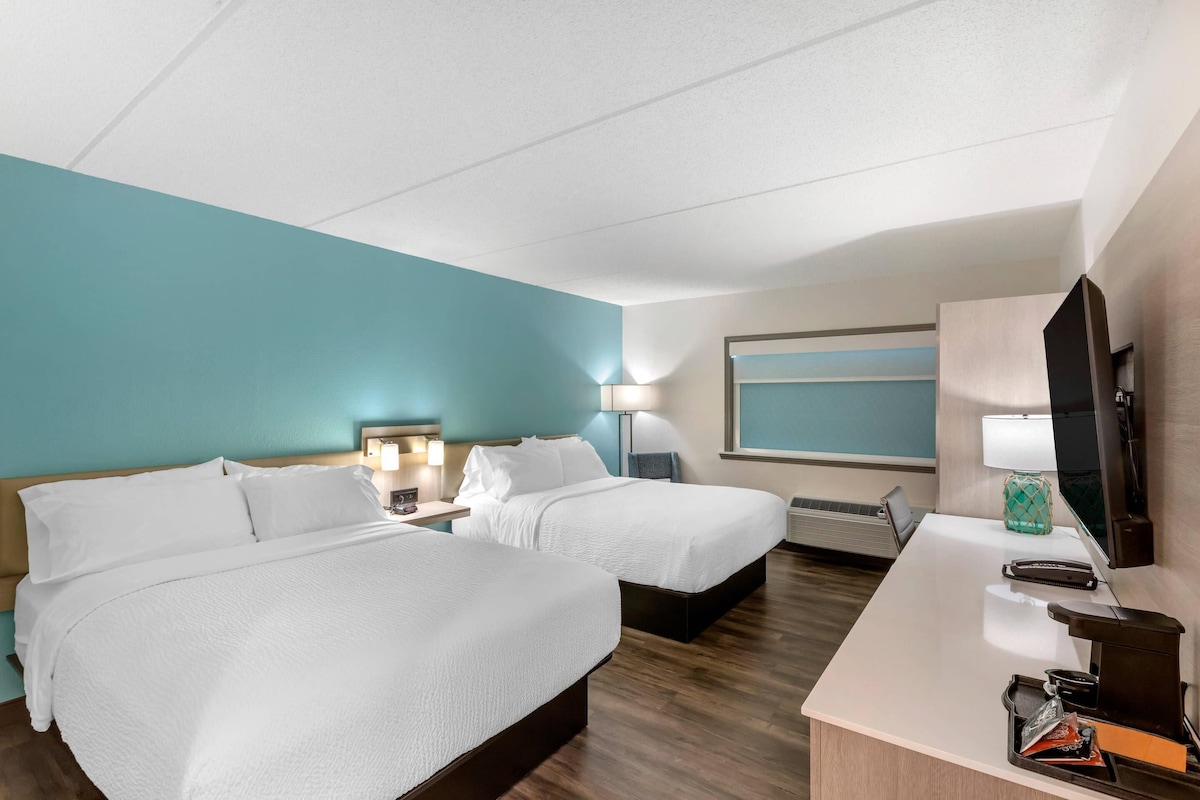 A hotel room with two beds, a desk, a TV, and a window.