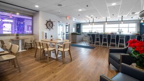 A modern interior with wooden flooring, a bar area with stools, and a seating area with tables and chairs. - The Harborview on Lake Michigan, an Ascend Collection Hotel (Port Washington)