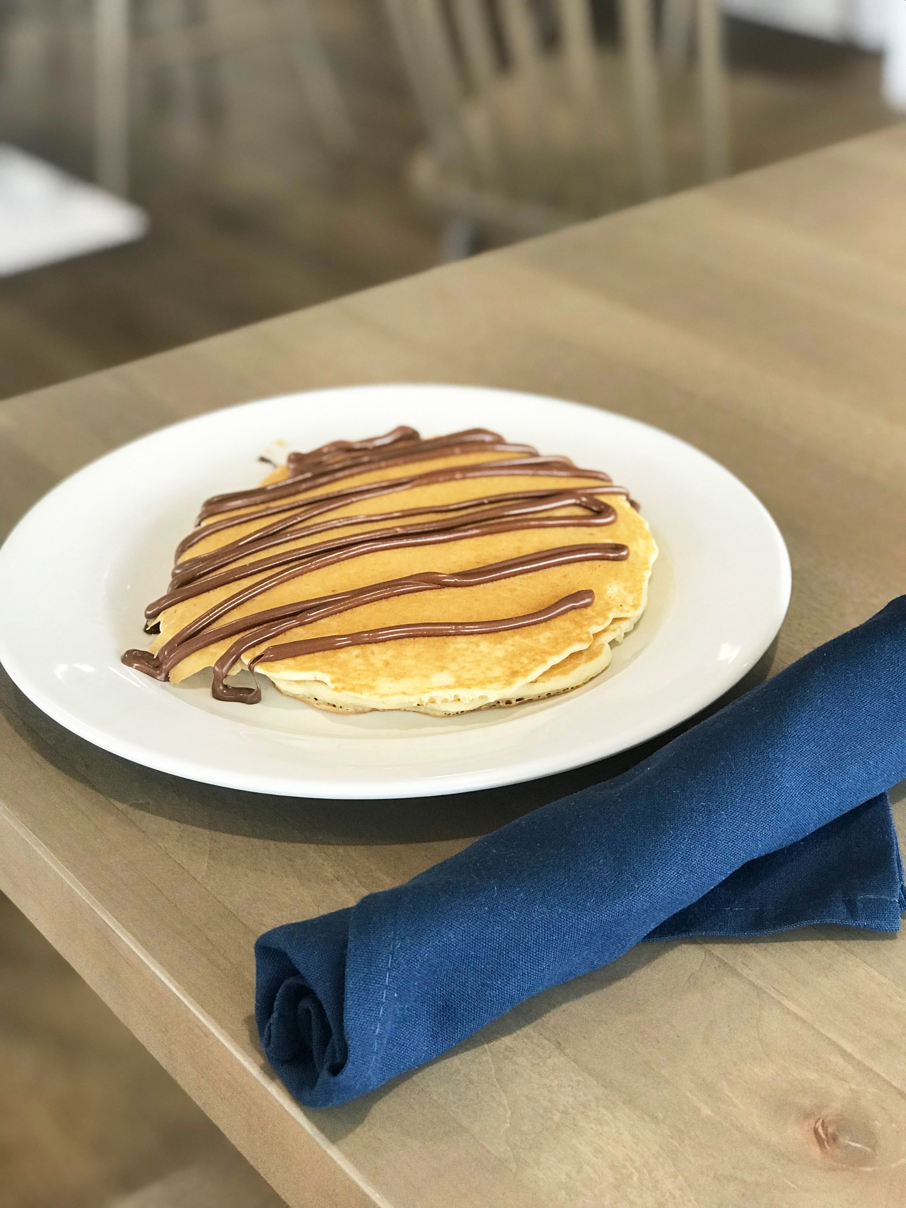 A plate of pancakes with chocolate drizzle on a wooden table.