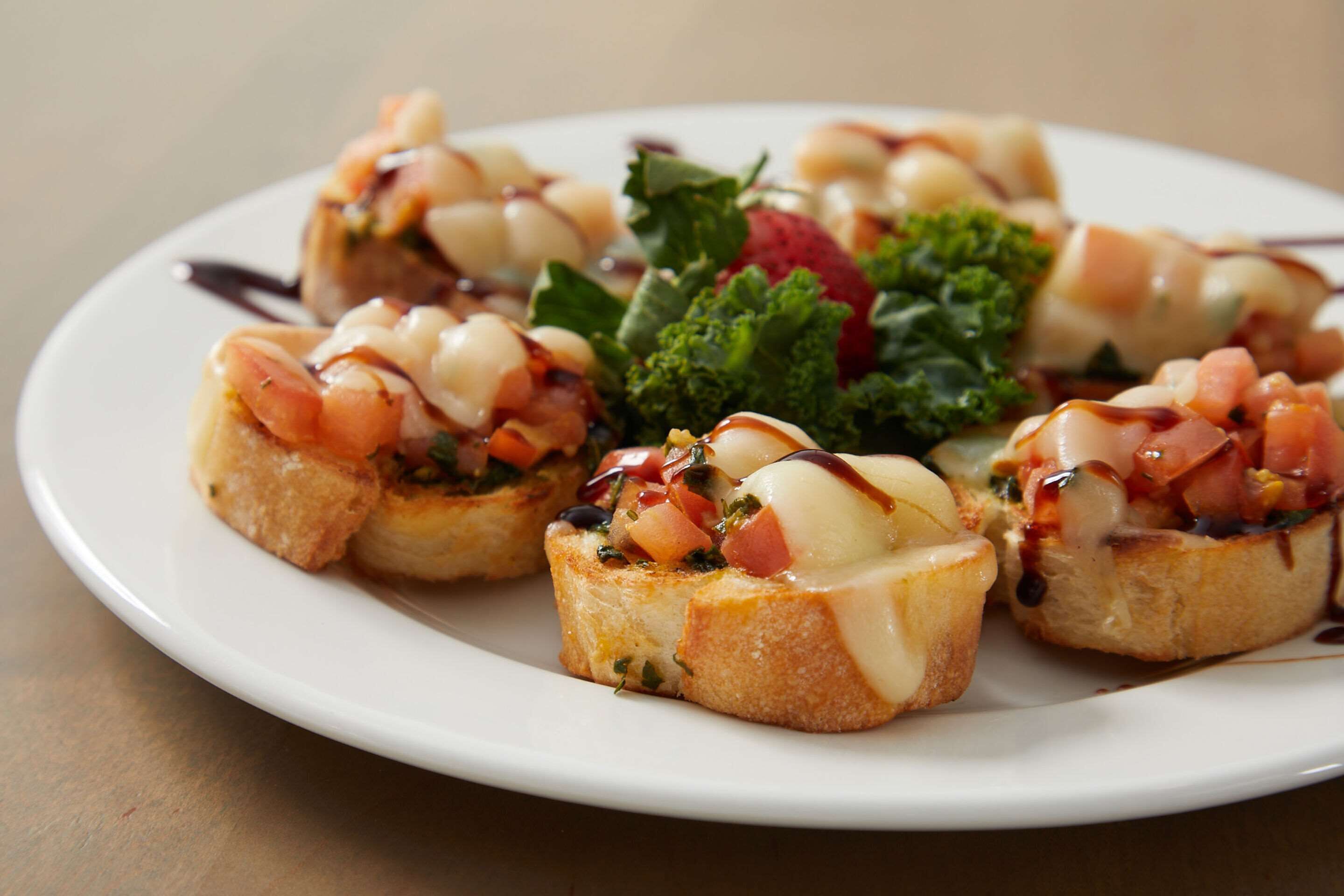 Un plato de bruschetta cubierto de tomates, albahaca y mozzarella, decorado con verdura de hoja y rociado con salsa.
