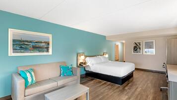 Una habitación de hotel con una cama, un sofá, una mesita de noche y un cuadro de una escena costera.