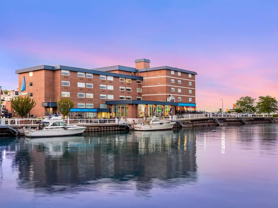A multi-story hotel with a docked boat, a waterfront view, and a clear sky.