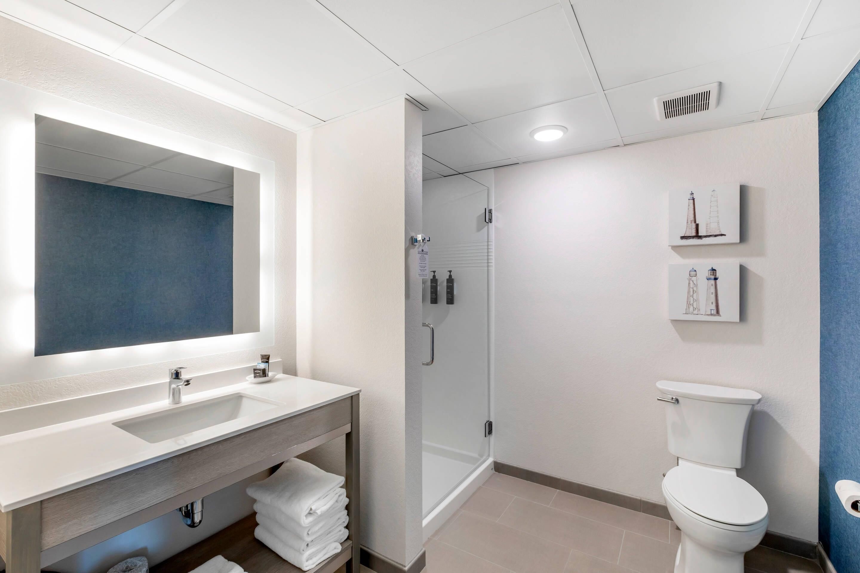 A modern bathroom with a large mirror, a sink, a toilet, and a shower area.