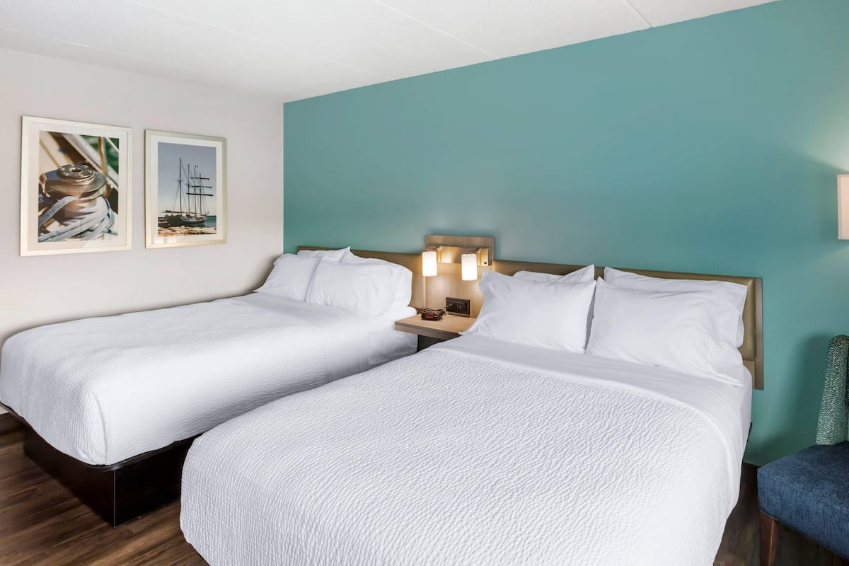 A hotel room with two beds, a teal accent wall, and framed nautical artwork.