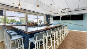 A bar area with a long counter, multiple stools, and hanging light fixtures. - The Harborview on Lake Michigan, an Ascend Collection Hotel (Port Washington)