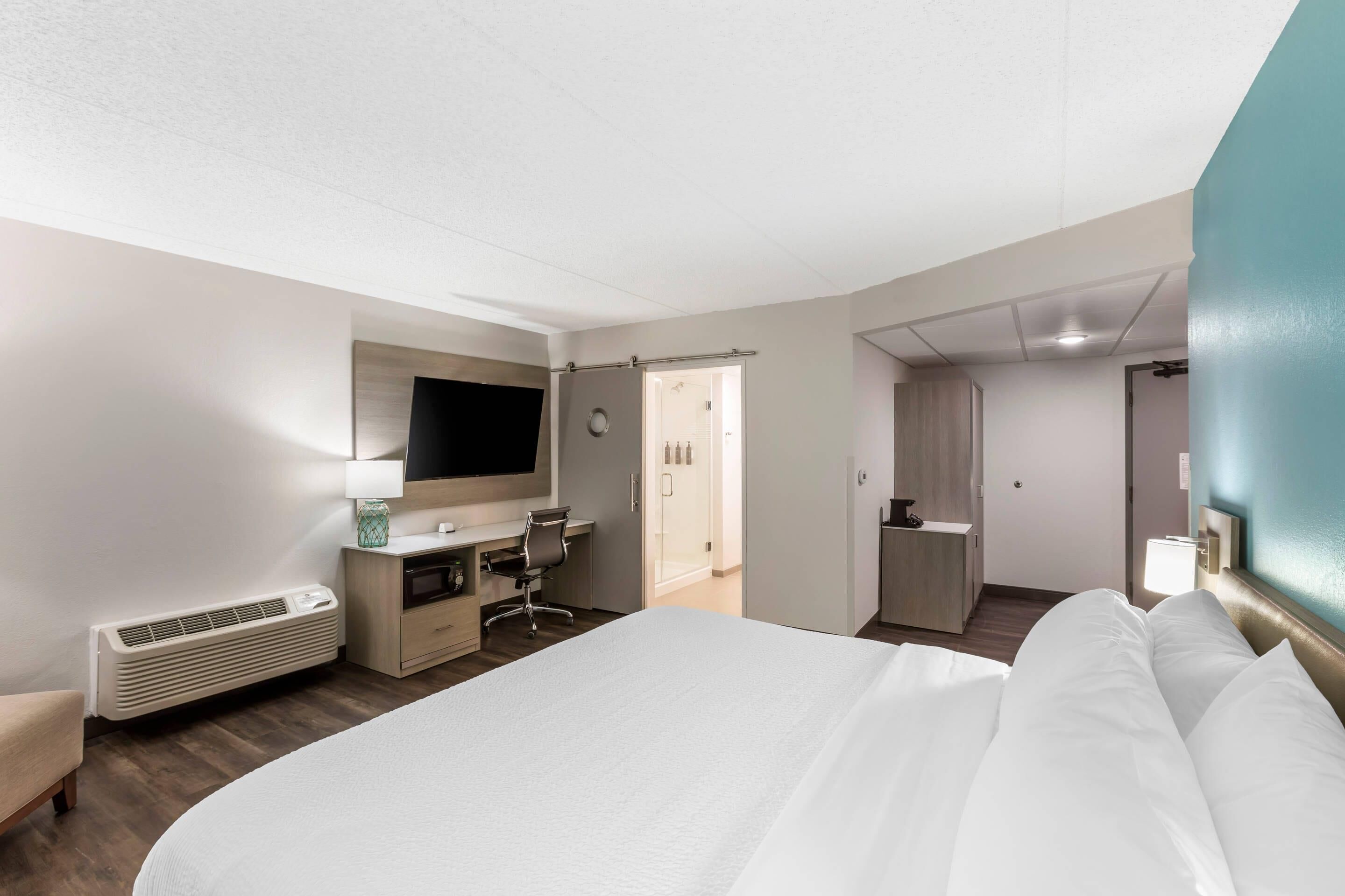 A hotel room with a large bed, a desk with a chair, a TV, and a bathroom door.