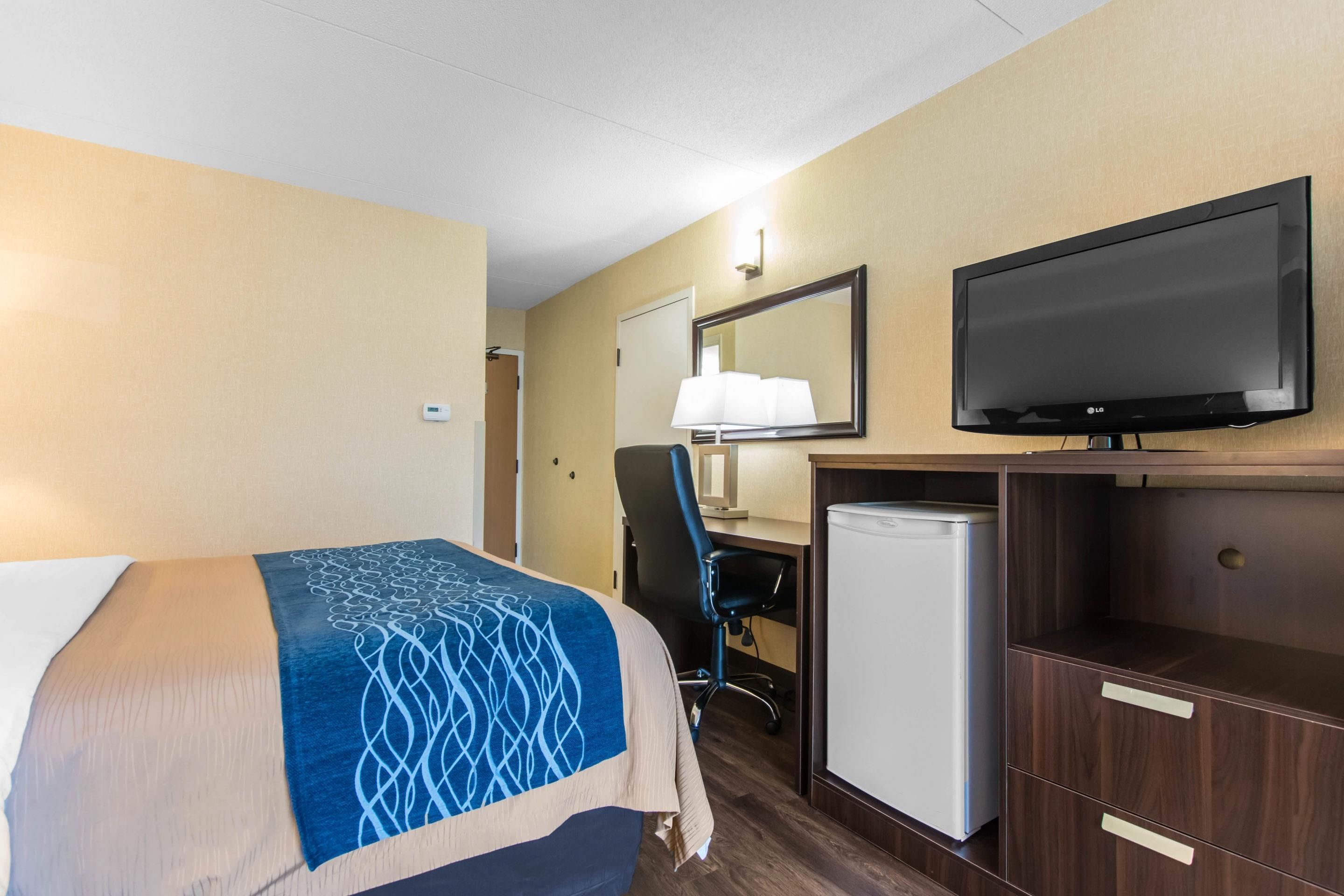 Una camera d'albergo con un letto, una scrivania con un computer, una televisione e un frigorifero.