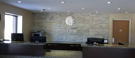 A hotel reception desk with a stone wall backdrop, a Dell computer, and a sign reading "Comfort Inn".