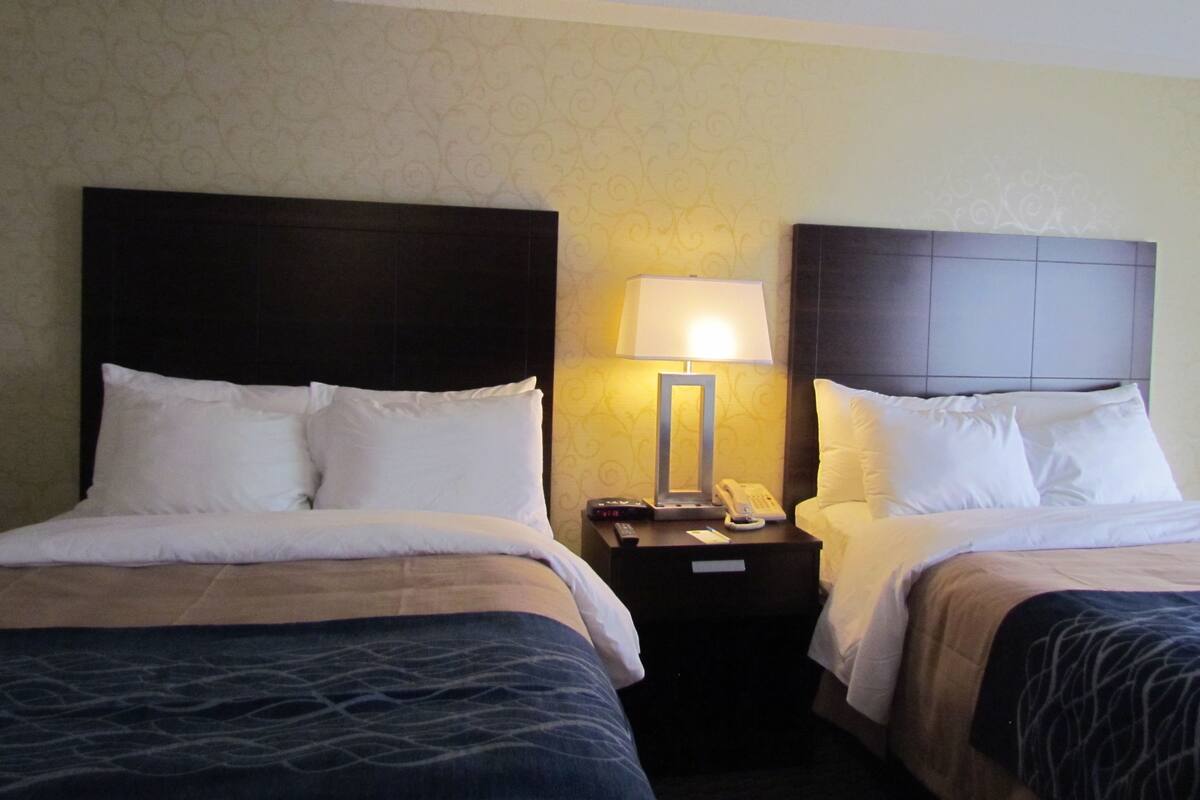 Een hotelkamer met twee bedden, een nachtkastje met een lamp en een telefoon.