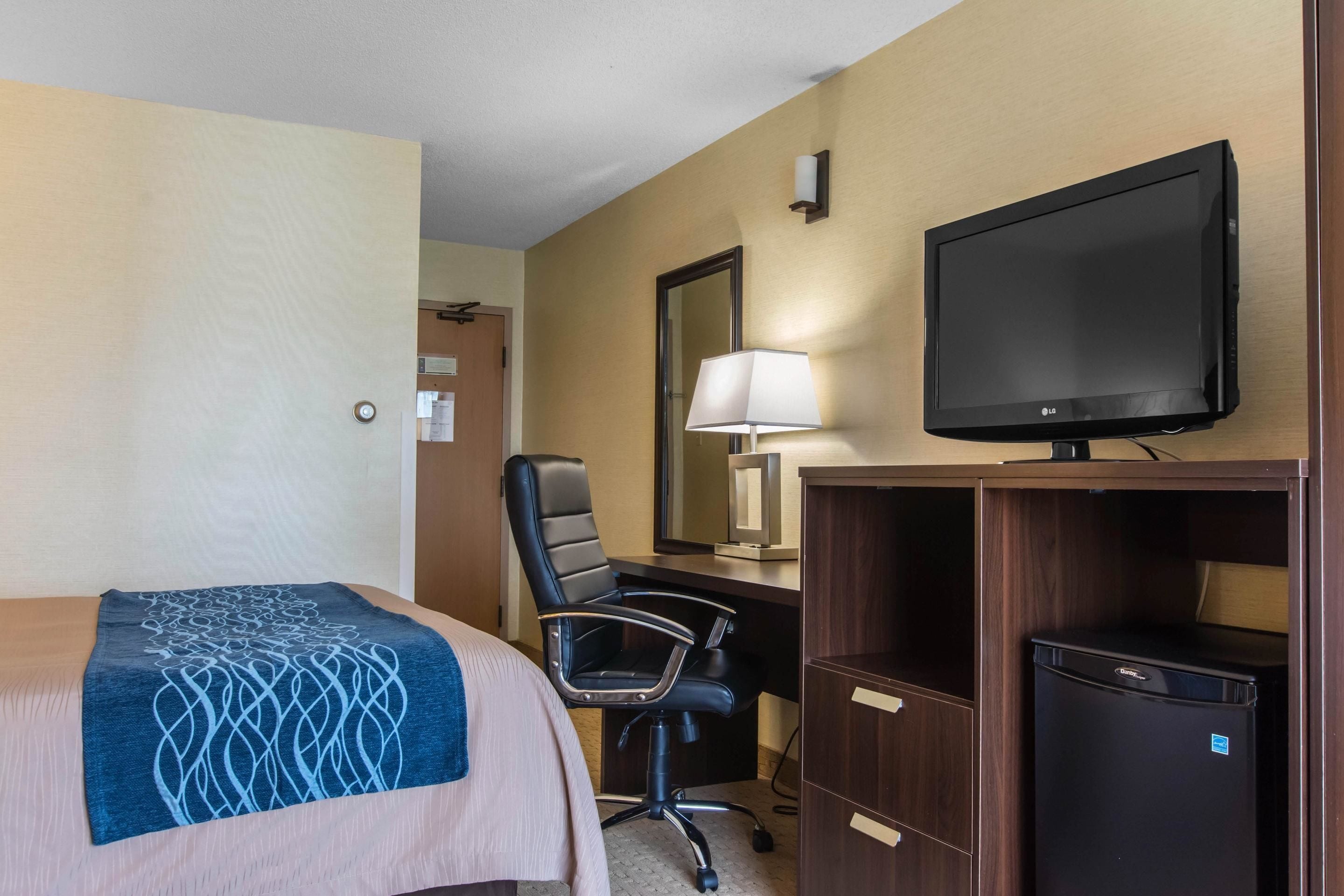 A hotel room with a bed, a desk, a chair, a television, and a refrigerator.