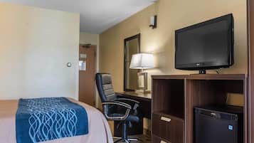 Una habitación de hotel con cama, escritorio, silla, televisor y refrigerador.