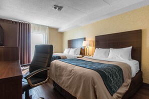 A hotel room with two beds, a desk, a chair, a lamp, and a window with curtains.