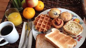 Un plateau de petit-déjeuner avec des gaufres, des muffins, des toasts et des fruits, accompagné d’une tasse de café et d’un verre de jus d’orange.