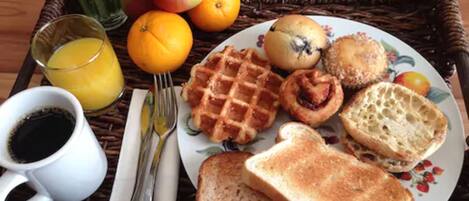 A breakfast tray with waffles, muffins, toast, and fruit, along with a cup of coffee and a glass of orange juice.