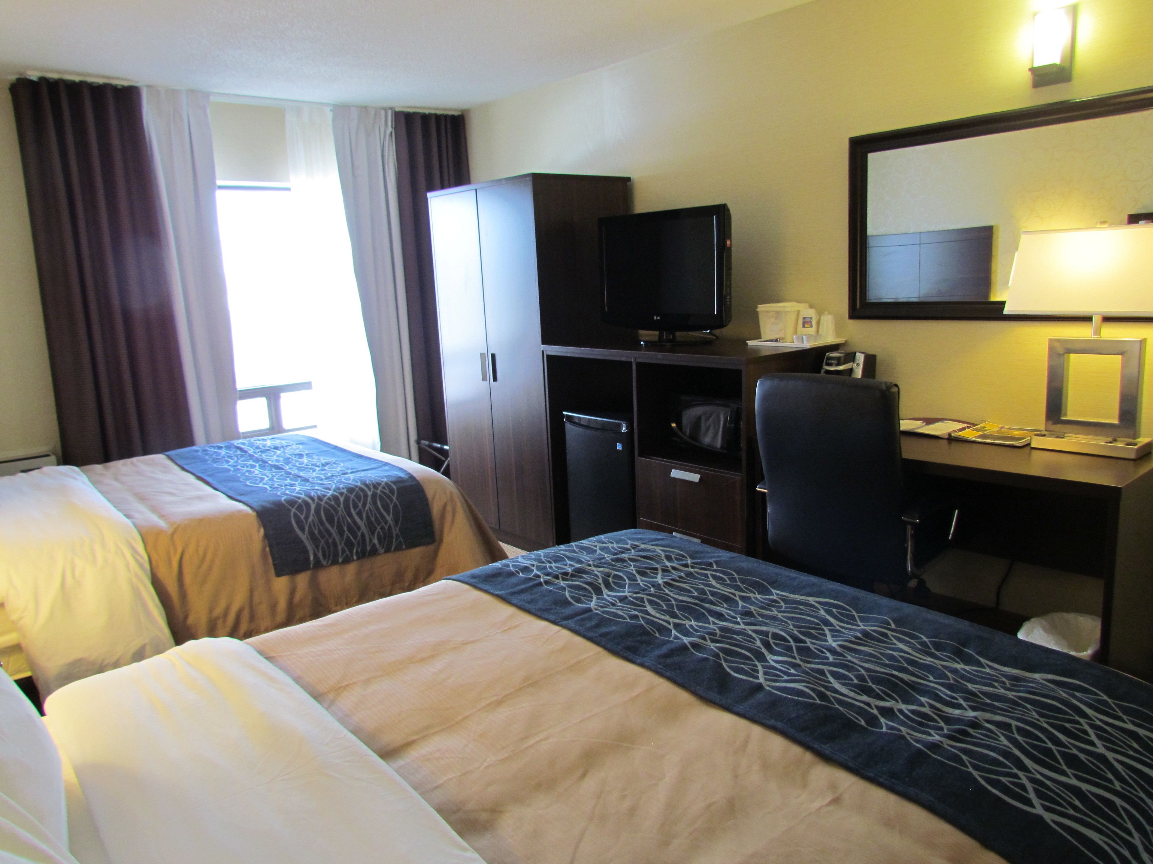 Una habitación de hotel con dos camas, un escritorio, un televisor y una lámpara de escritorio.