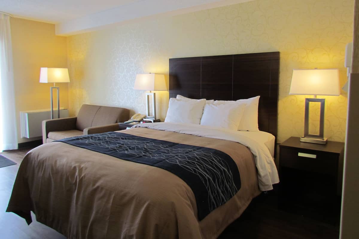 Een hotelkamer met een groot bed, twee nachtkastjes met lampen, een stoel en een telefoon.