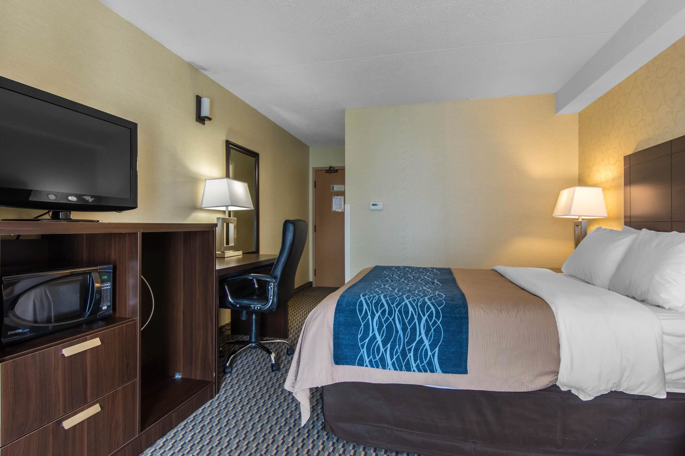 A hotel room with a bed, a desk with a computer, a TV, a microwave, and two lamps.