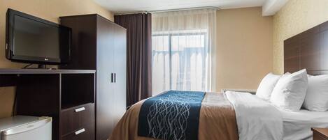A hotel room with a bed, a television, a wardrobe, and a small refrigerator.