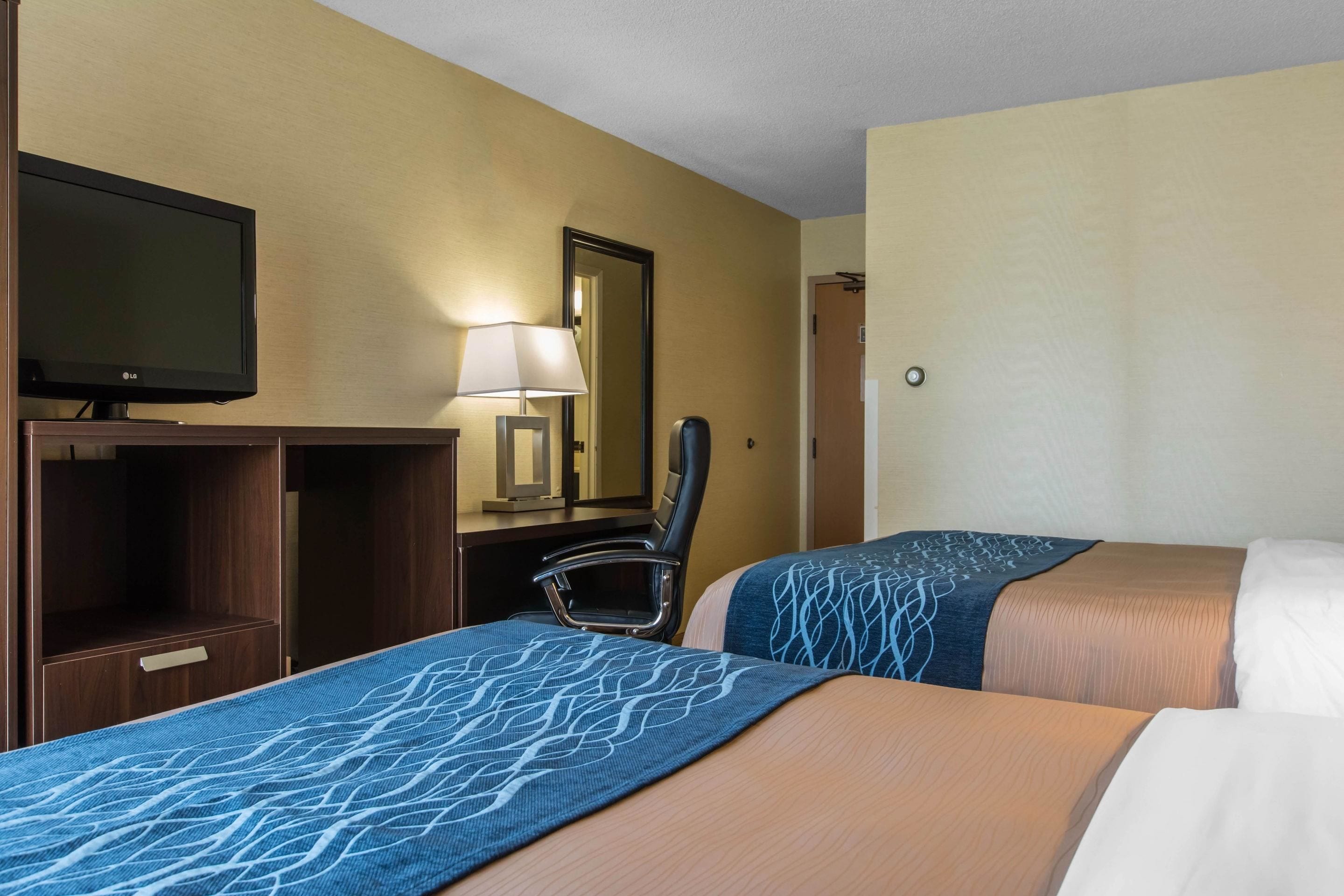 A hotel room with two beds, a TV, a desk with a lamp, and a mirror.